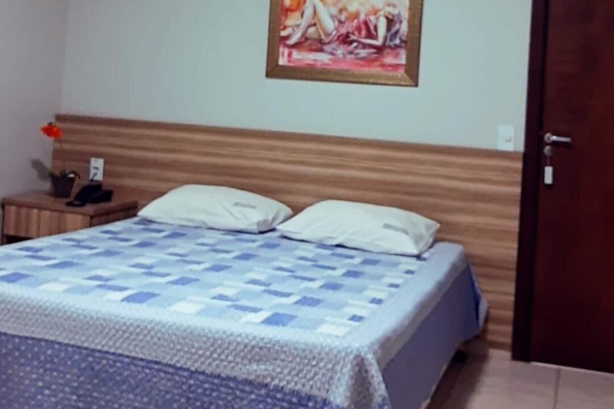 Een slaapkamer met een bed, een nachtkastje, een schilderij aan de muur en een deur.