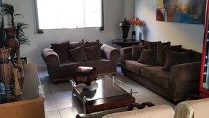 A spacious living room with a large window, two sofas, a coffee table, and a decorative vase. - Monte Castro Executive Hotel (Araguari)
