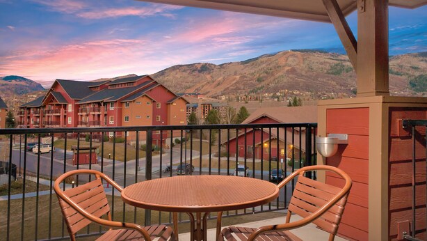 A balcony with wicker chairs and a table, overlooking a town with red buildings and mountains in the background. - WorldMark Steamboat Springs (Steamboat Springs)