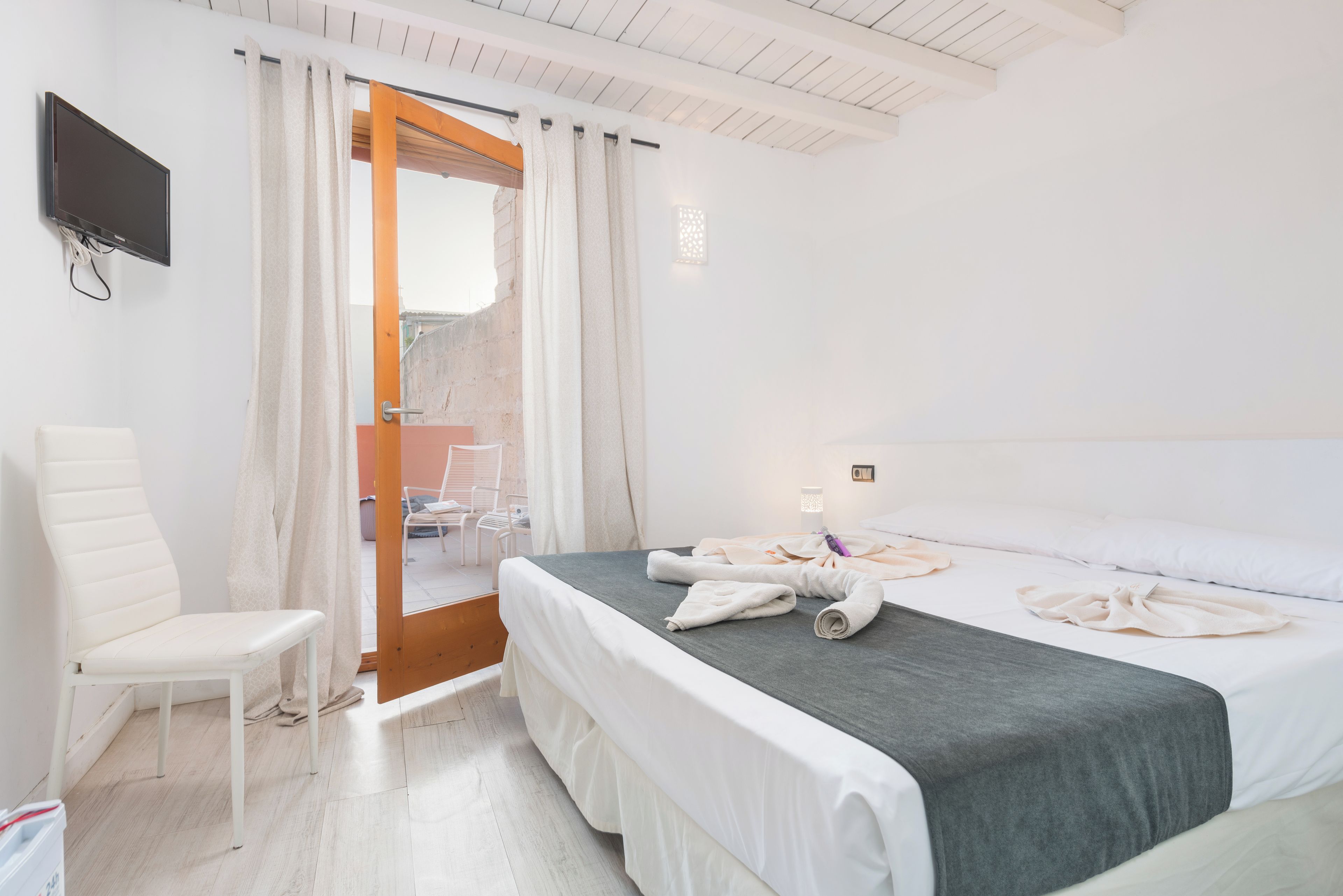 Een hotelkamer met een bed, een stoel, een televisie en een deur naar een buitenruimte.