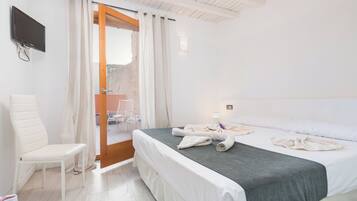 Een hotelkamer met een bed, een stoel, een televisie en een deur naar een buitenruimte.
