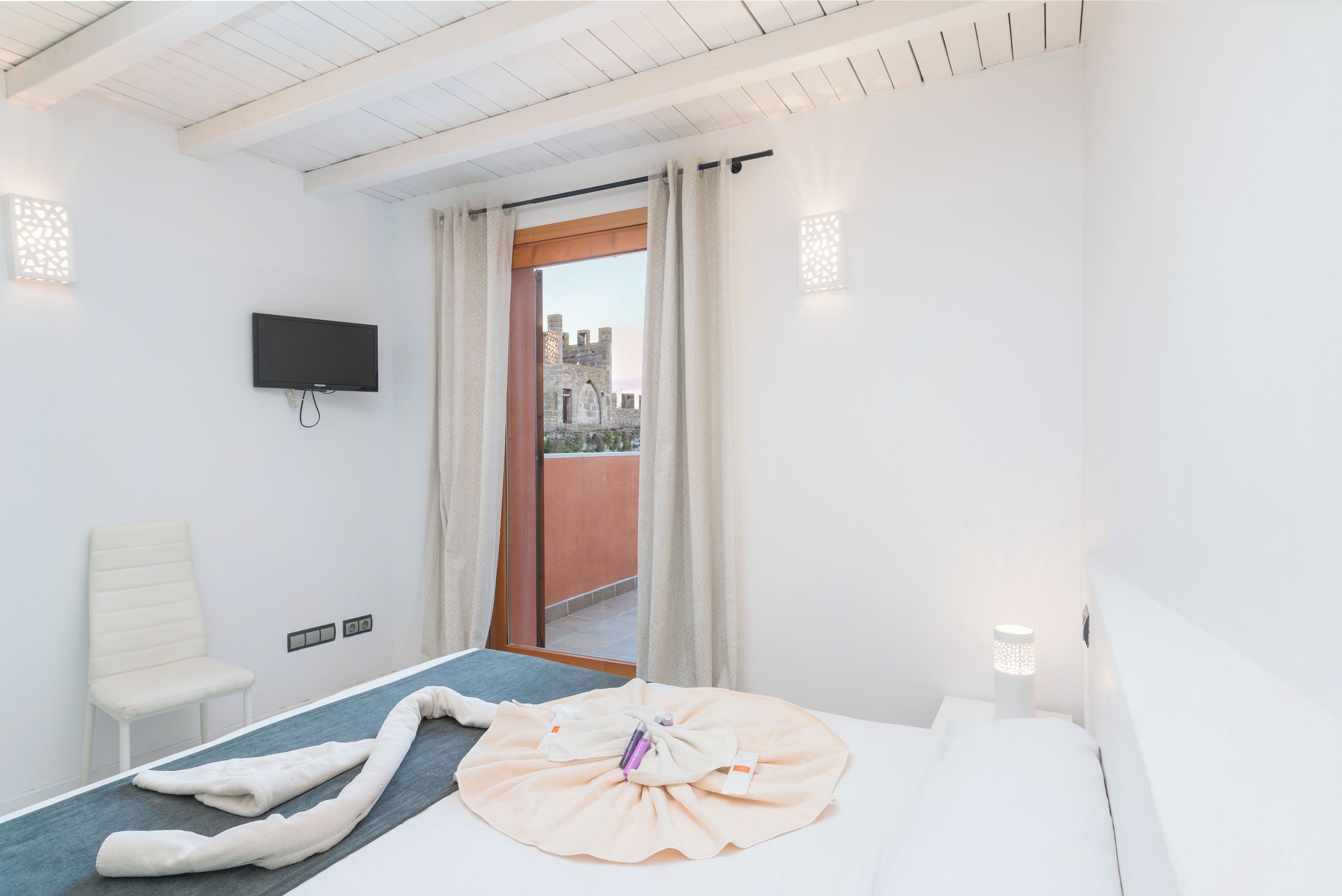 Una habitación de hotel con cama, televisor, una silla y vista a un edificio desde la ventana.