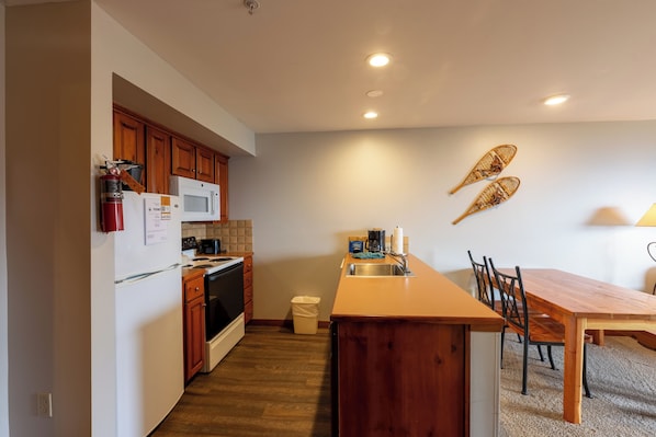 A modern kitchen with wooden cabinets, a microwave, and a wooden dining table with chairs. - Highland House (Snowshoe)