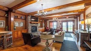 A spacious living room with wooden beams, a fireplace, leather furniture, and a large chandelier. - Highland House (Snowshoe)