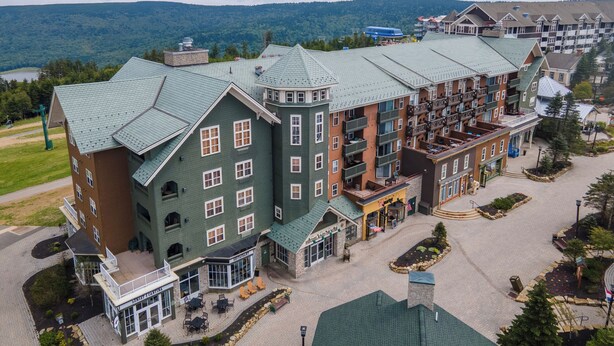 A large hotel with multiple floors, a central courtyard, and a view of the surrounding mountains. - Highland House (Snowshoe)