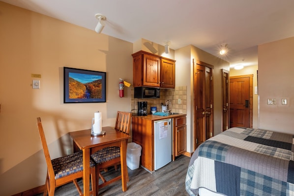 A compact hotel room with a kitchenette, a dining area, and a bed. - Highland House (Snowshoe)