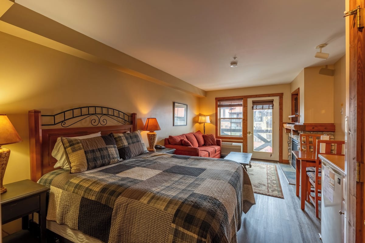 A bedroom with a large bed, a wooden headboard, two bedside tables with lamps, a red sofa, and a wooden desk with a chair.