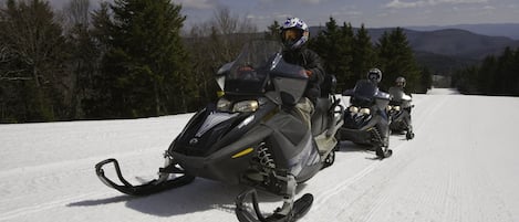 A snowmobile on a snowy path with a forest and mountains in the background.