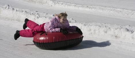 Una persona con un traje de nieve rosa con lunares surfeando un tubo de nieve rojo en una pendiente nevada.