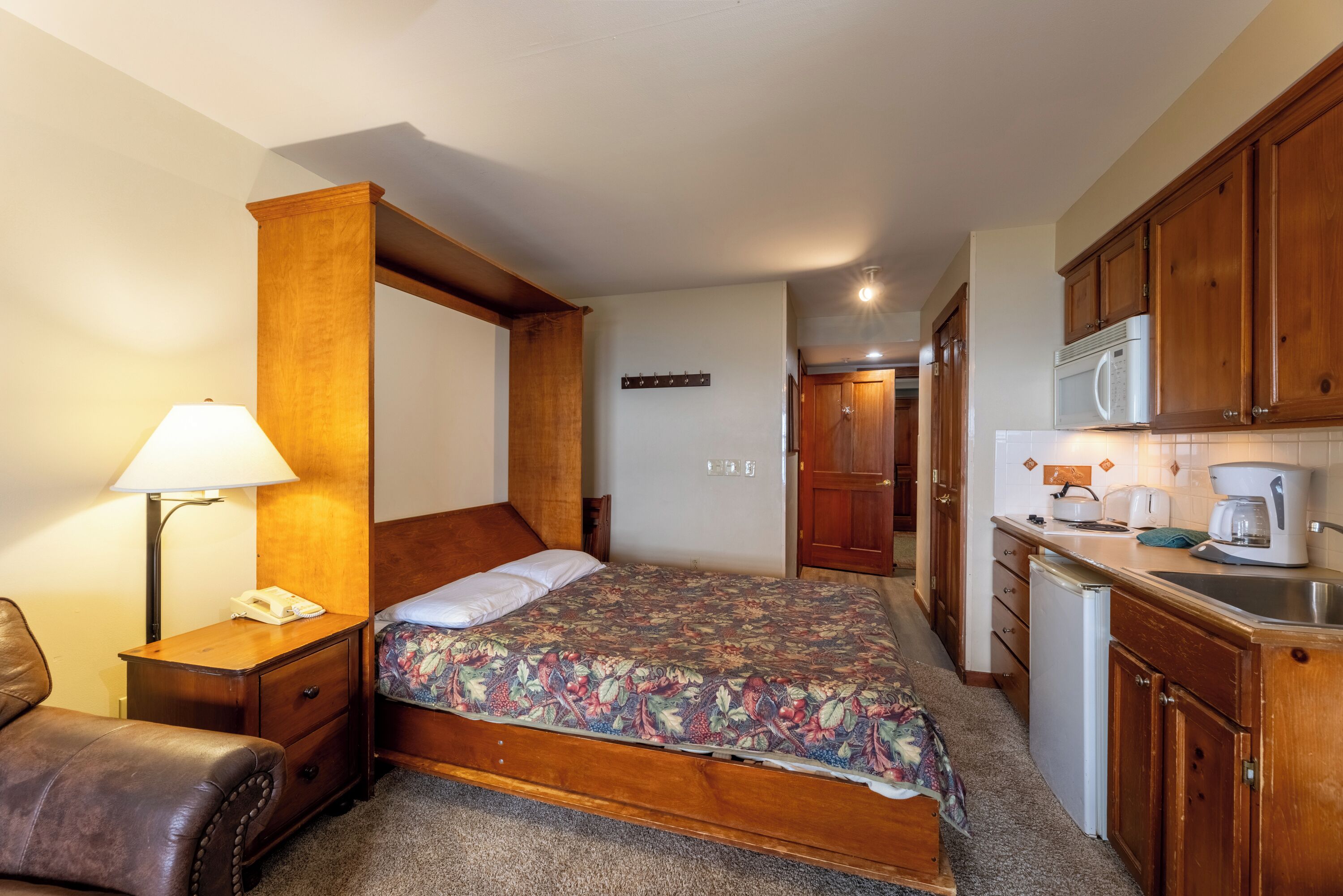 A bedroom with a bed, bedside table, lamp, and a small desk with a chair.