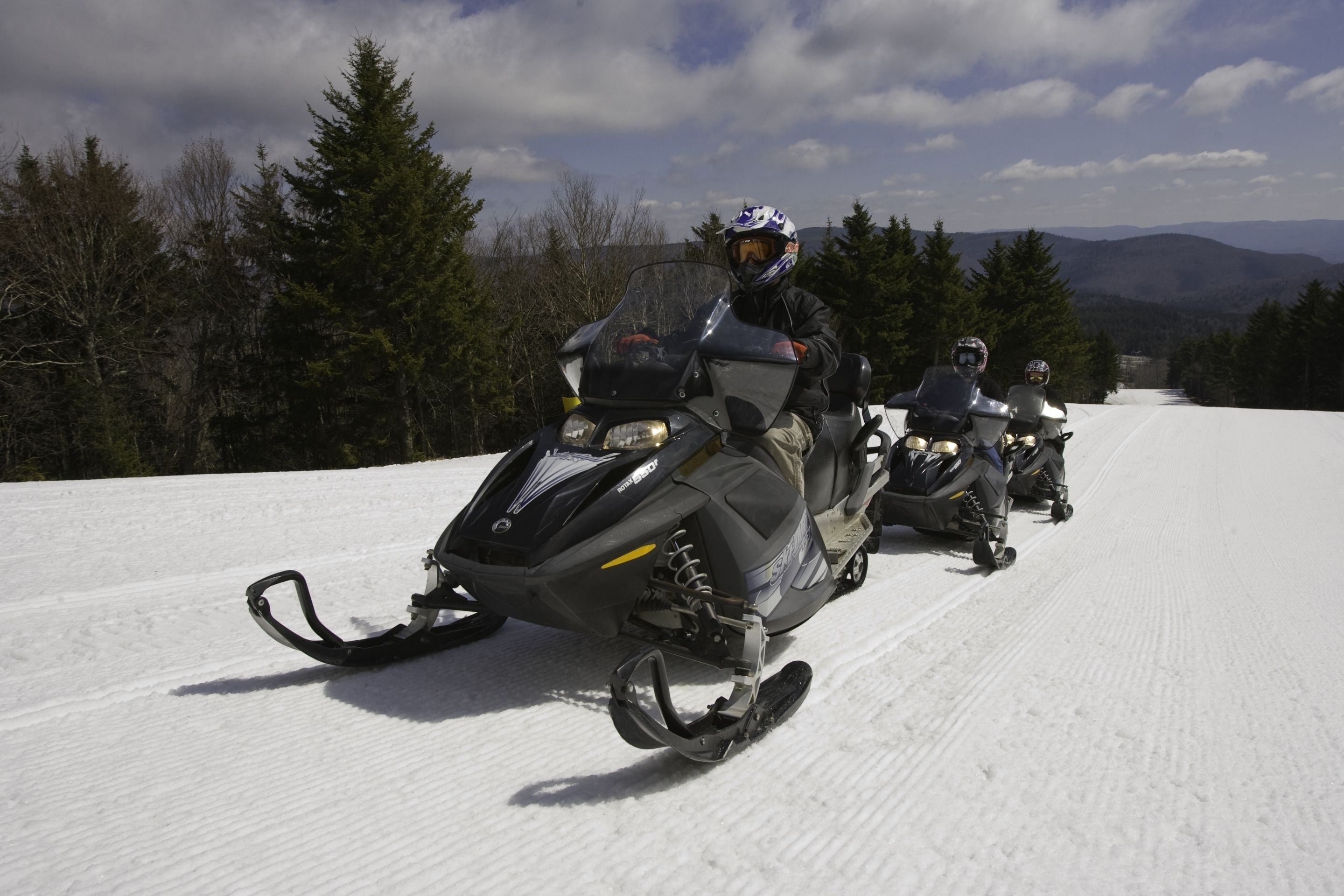 A snowmobile on a snowy path with a forest and mountains in the background.