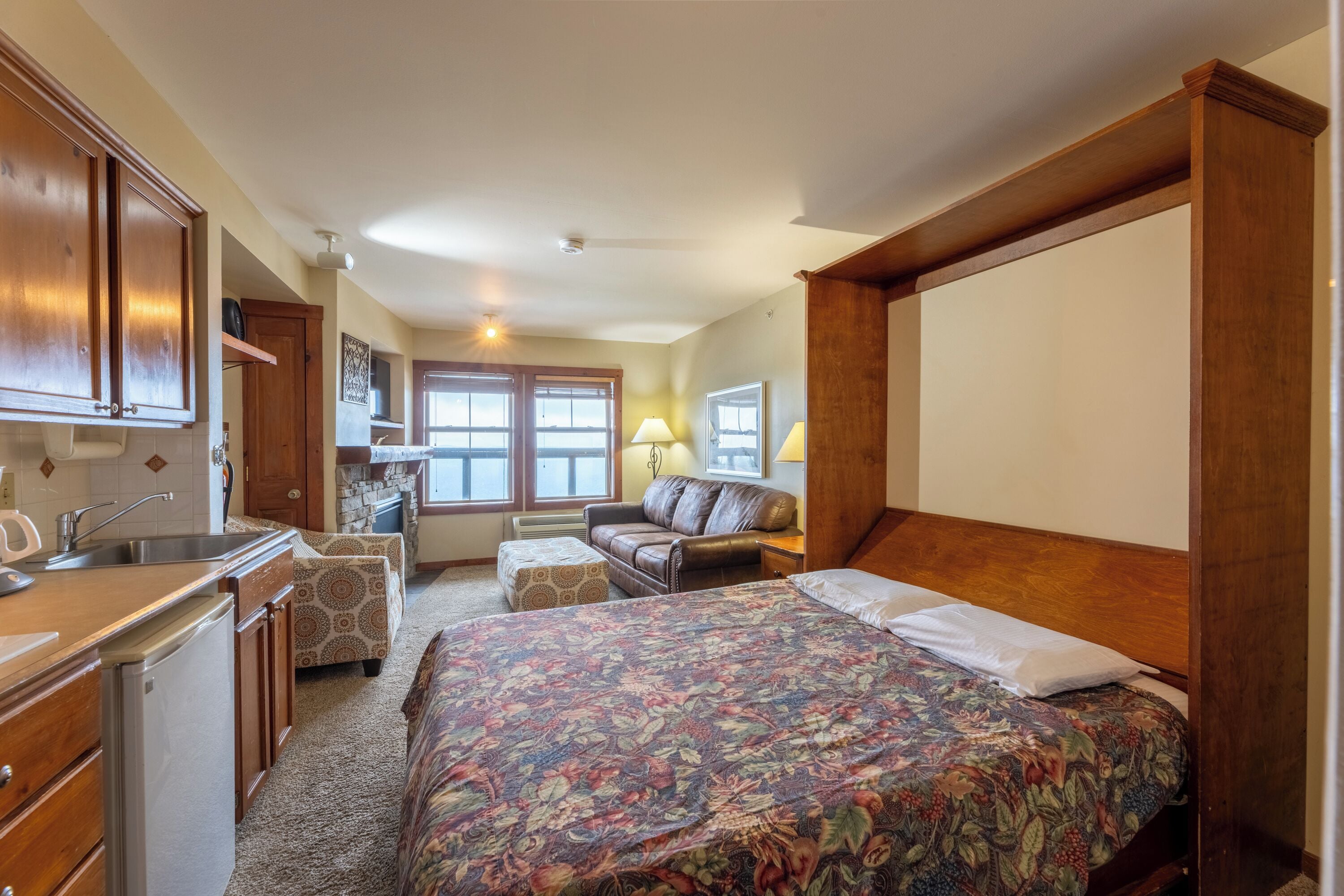 A bedroom with a large bed, a sofa, a dining area, and a kitchen.