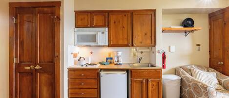 A compact kitchen with wooden cabinets, a microwave, a refrigerator, and a sink.