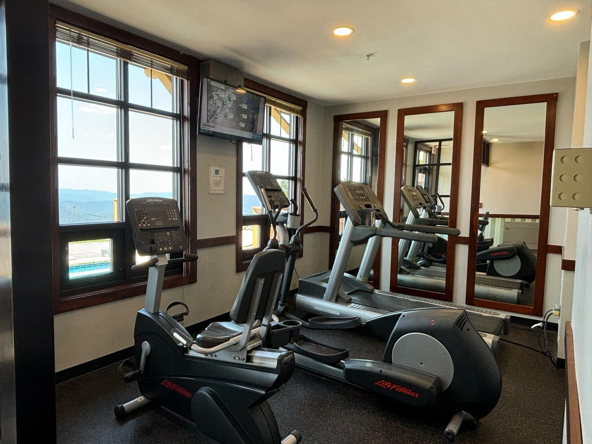 A gym with treadmills, ellipticals, and a TV mounted on the wall.