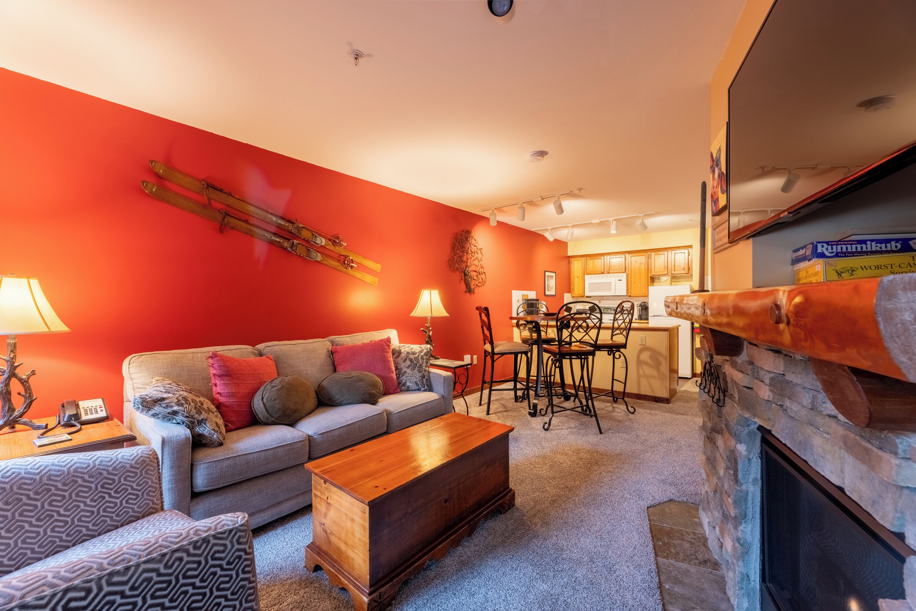 A living room with a red wall, a fireplace, a sofa, a coffee table, and a dining area with chairs and a table.