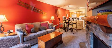 A living room with a red wall, a fireplace, a sofa, a coffee table, and a dining area with chairs and a table.
