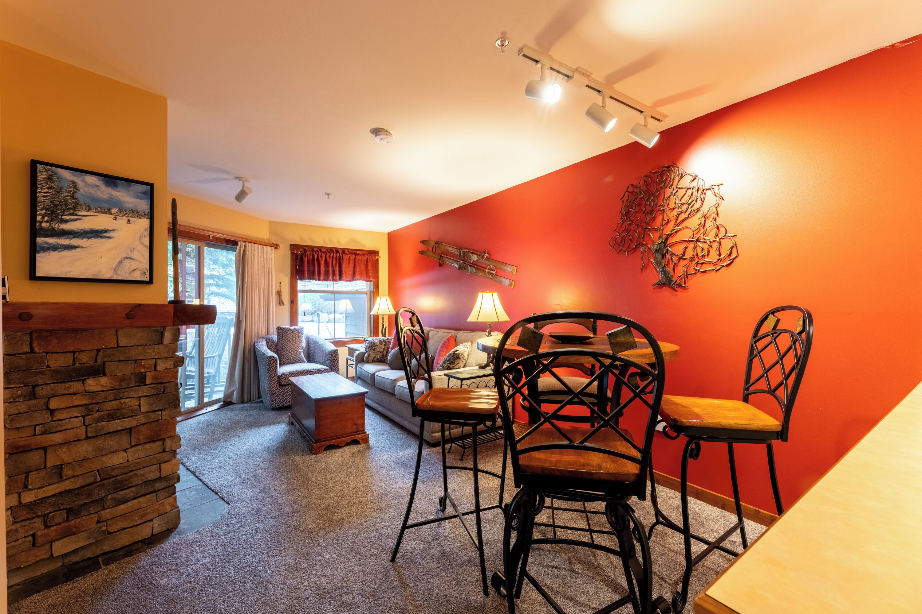 A cozy living room with a stone fireplace, a dining area with two chairs, a sofa, and a table.