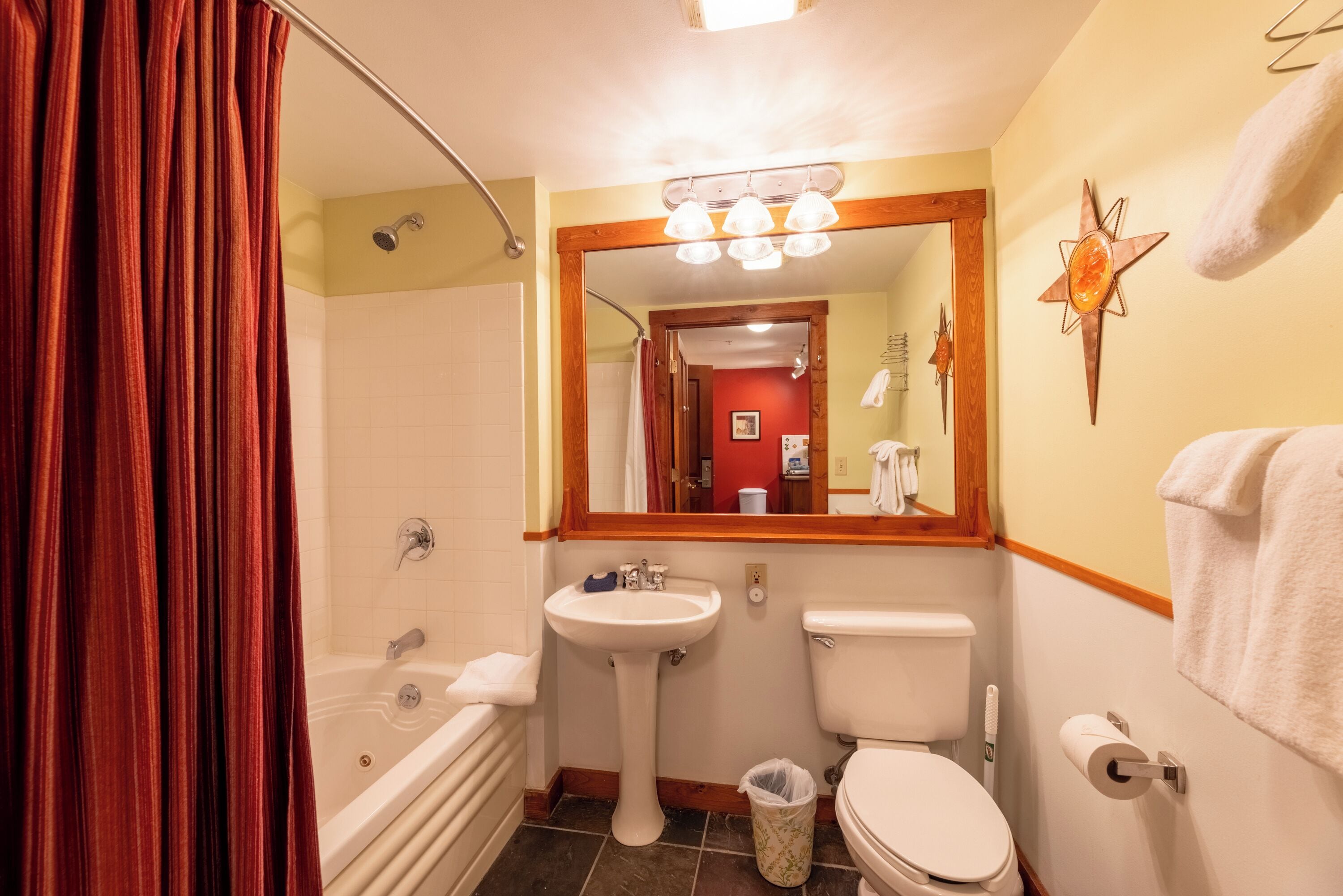 Een badkamer met een badkuip, wastafel, toilet en een spiegel boven de wastafel.