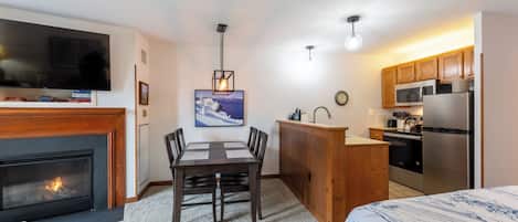 Un espacio habitable compacto con chimenea, una mesa de comedor, kitchenette y cama.