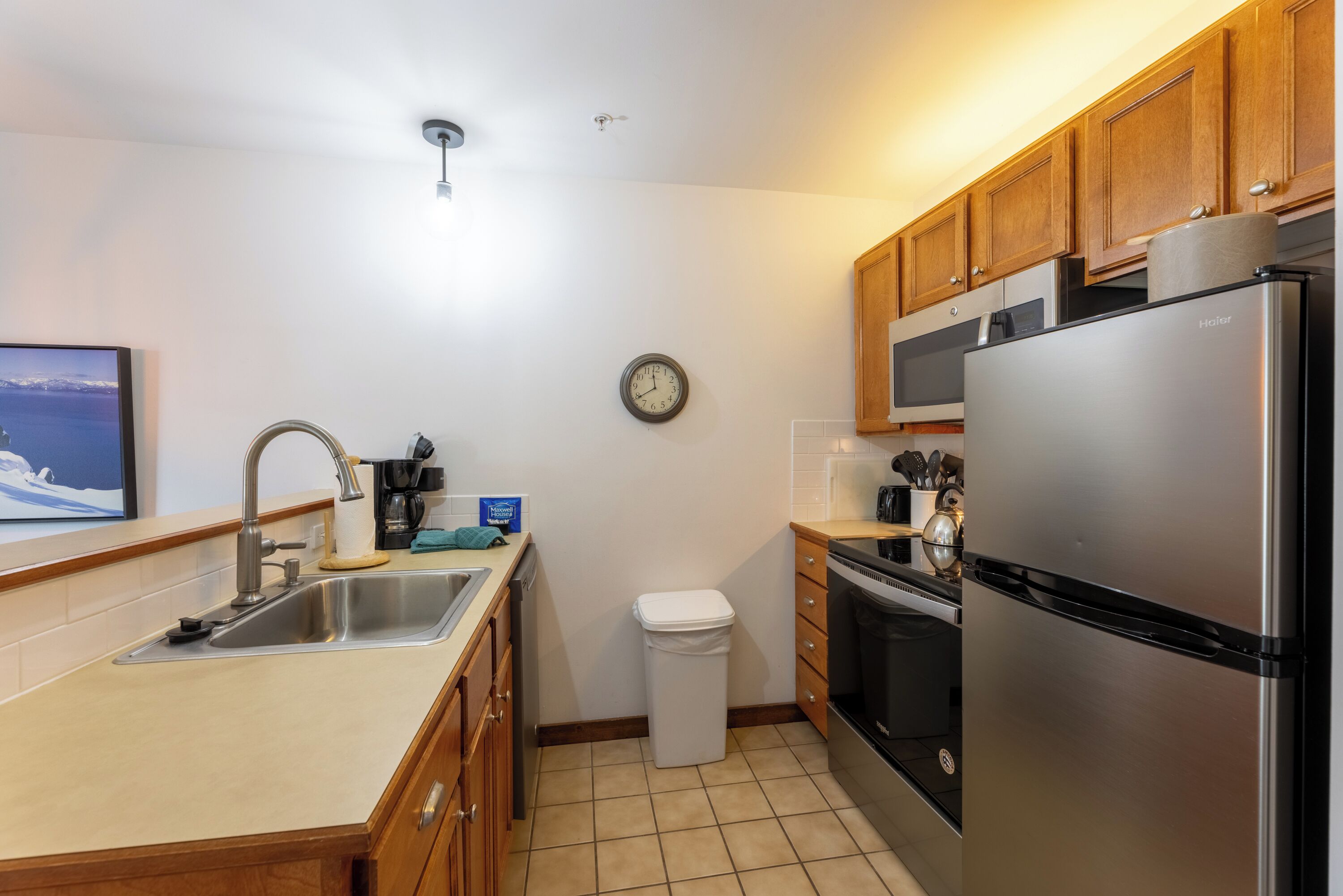 Cocina moderna con electrodomésticos de acero inoxidable, armarios de madera, un lavabo y un reloj en la pared.