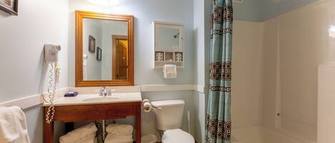 A bathroom with a wooden vanity, a toilet, a sink, a mirror, and a shower with a patterned curtain.