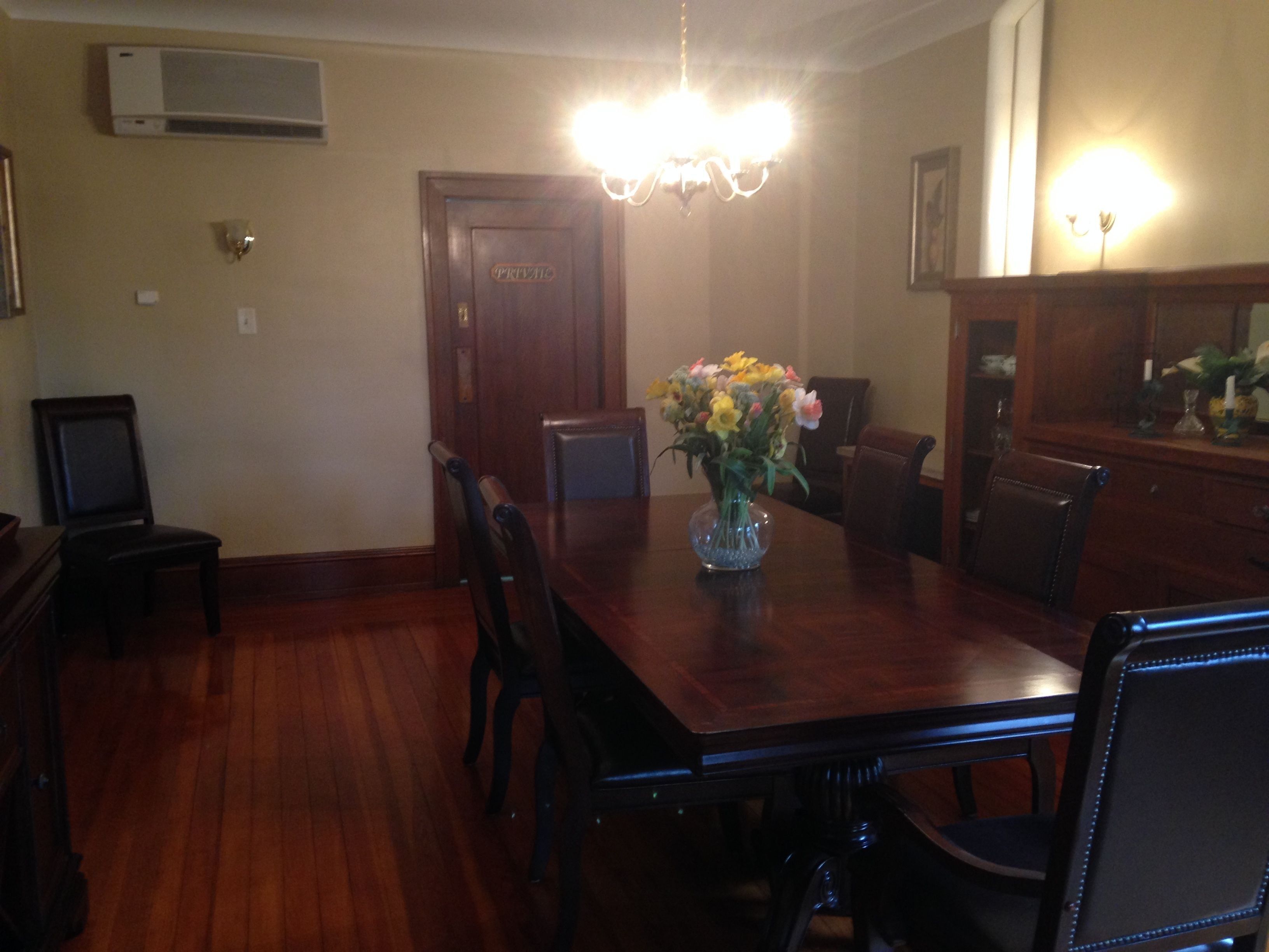 Un comedor con mesa de madera, sillas, una araña y un jarrón con flores.