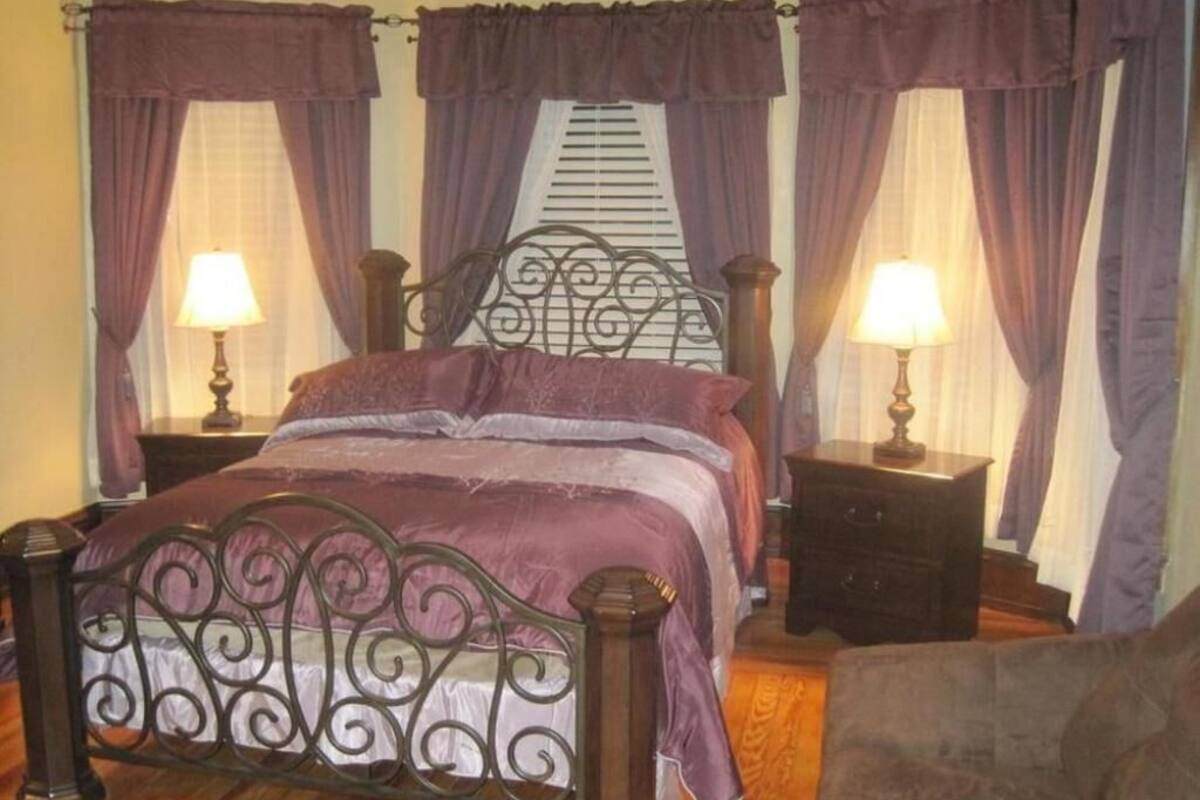 A bedroom with a metal bed frame, two bedside tables with lamps, and purple curtains.