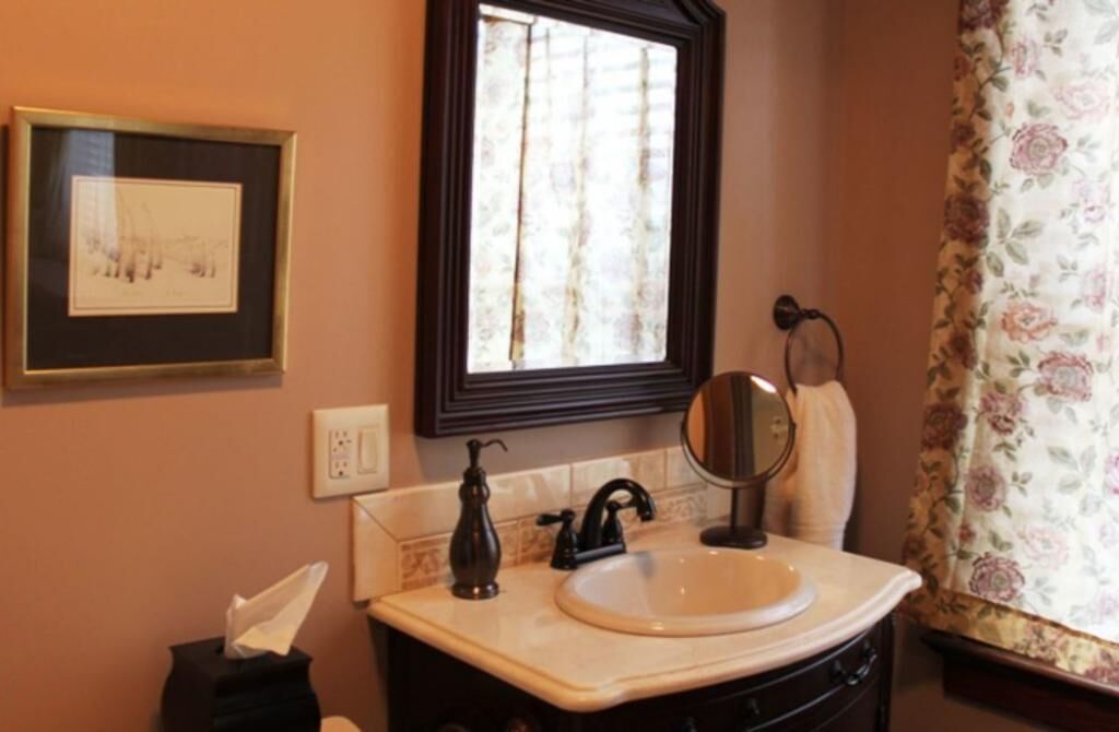 Une salle de bain avec un tableau encadré, une fenêtre donnant sur un paysage, un lavabo, un miroir et un porte-serviettes.