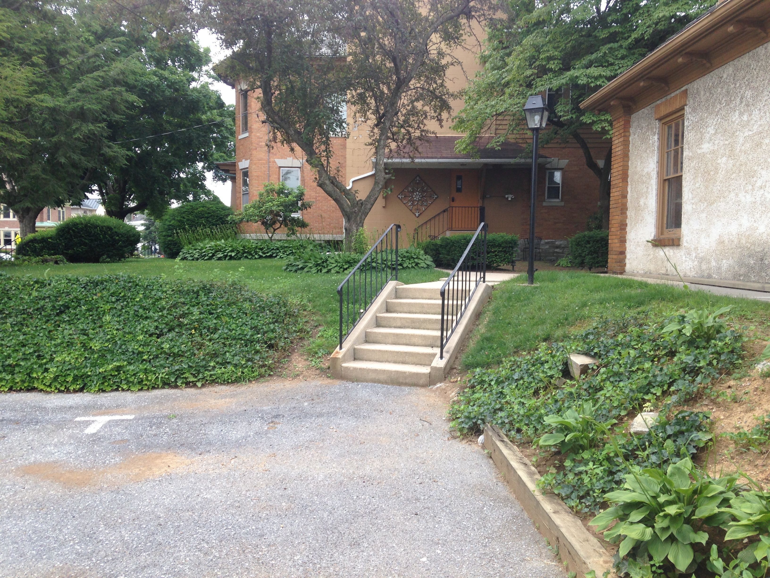 A residential building with a front entrance, a staircase leading to the entrance, and a well-maintained garden area.