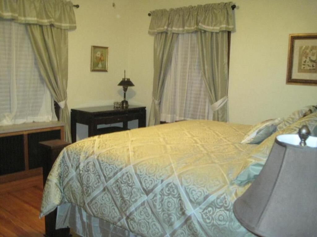 A bedroom with a bed, curtains, a lamp, and a picture on the wall.