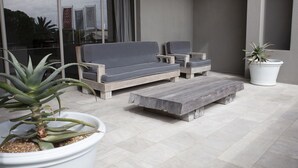 An outdoor seating area with a sofa and chairs, a wooden table, and potted plants. - Atlantic Beach Hotel (Cape Town)
