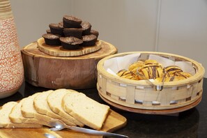 A wooden cutting board with sliced bread, a wooden cake stand with brownies, and a basket with cookies. - Atlantic Beach Hotel (Cape Town)