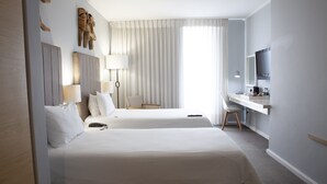 A hotel room with two beds, a desk, a chair, a TV, and a window with curtains. - Atlantic Beach Hotel (Cape Town)