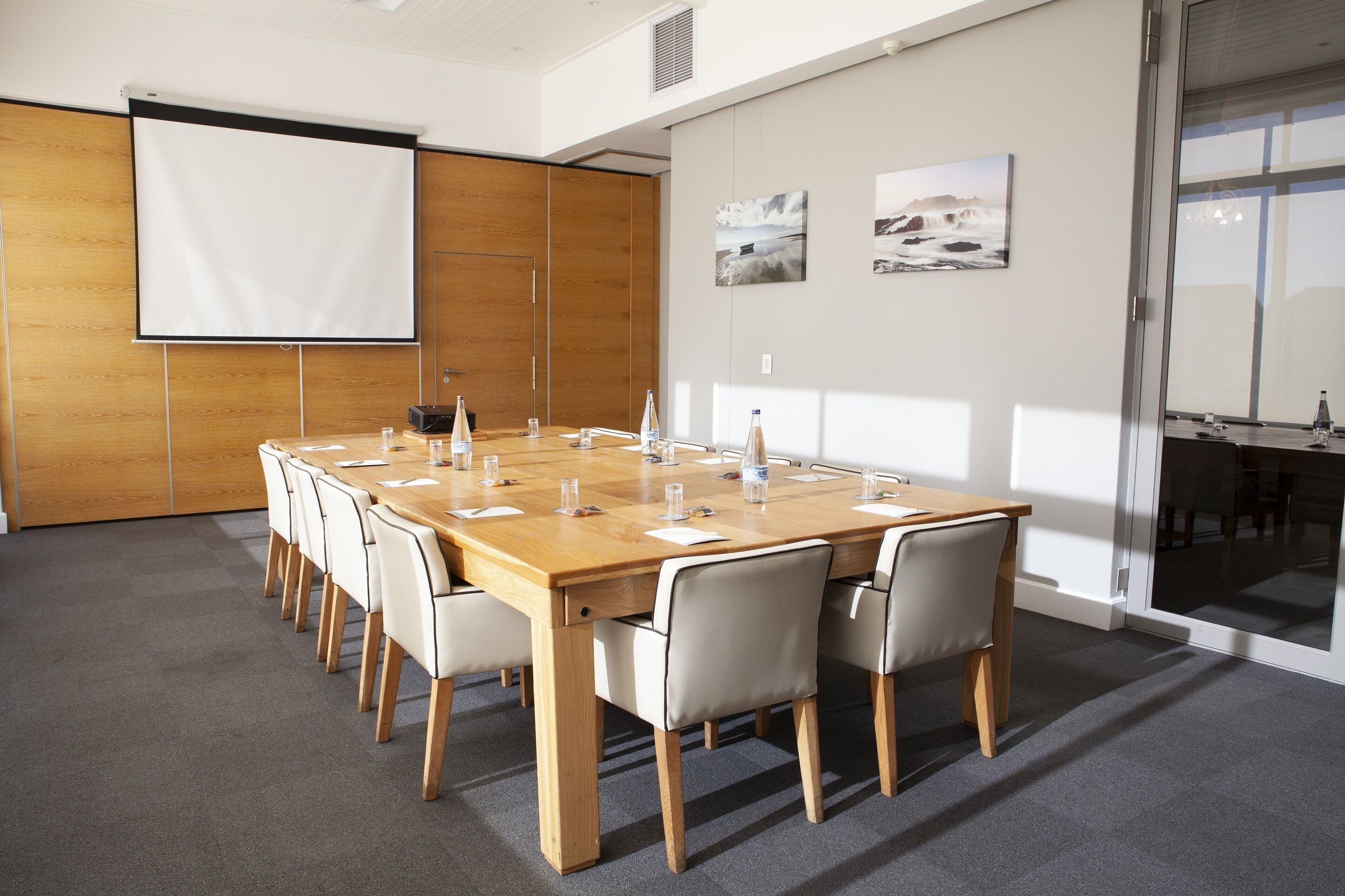 A conference room with a large table, chairs, a projector screen, and artwork on the walls.