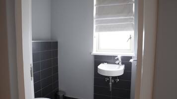 A bathroom with a white sink, a window with blinds, and dark tiled walls.