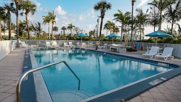 A swimming pool with lounge chairs and umbrellas, surrounded by palm trees.