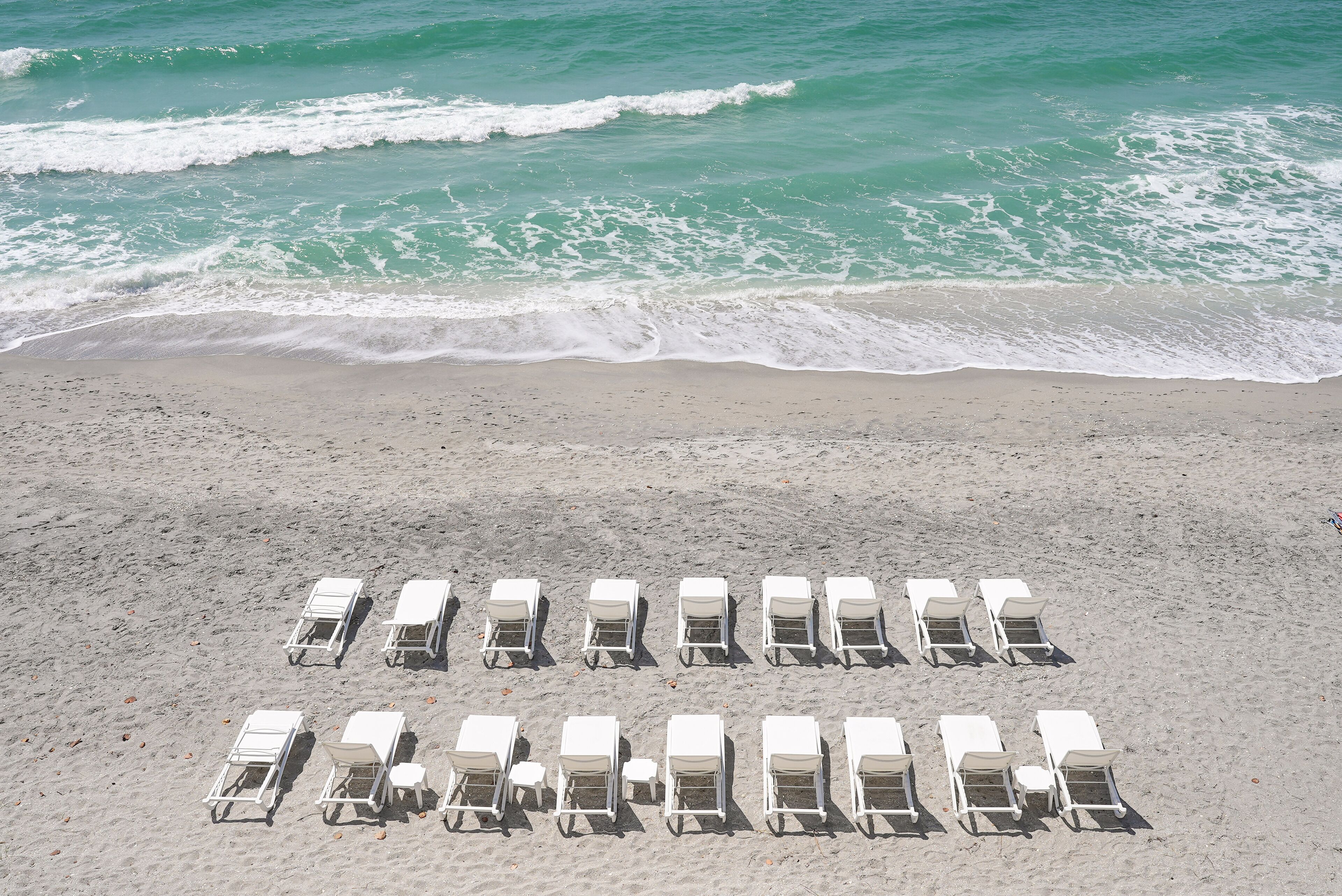 A beach with rows of white lounge chairs and a sandy shore.