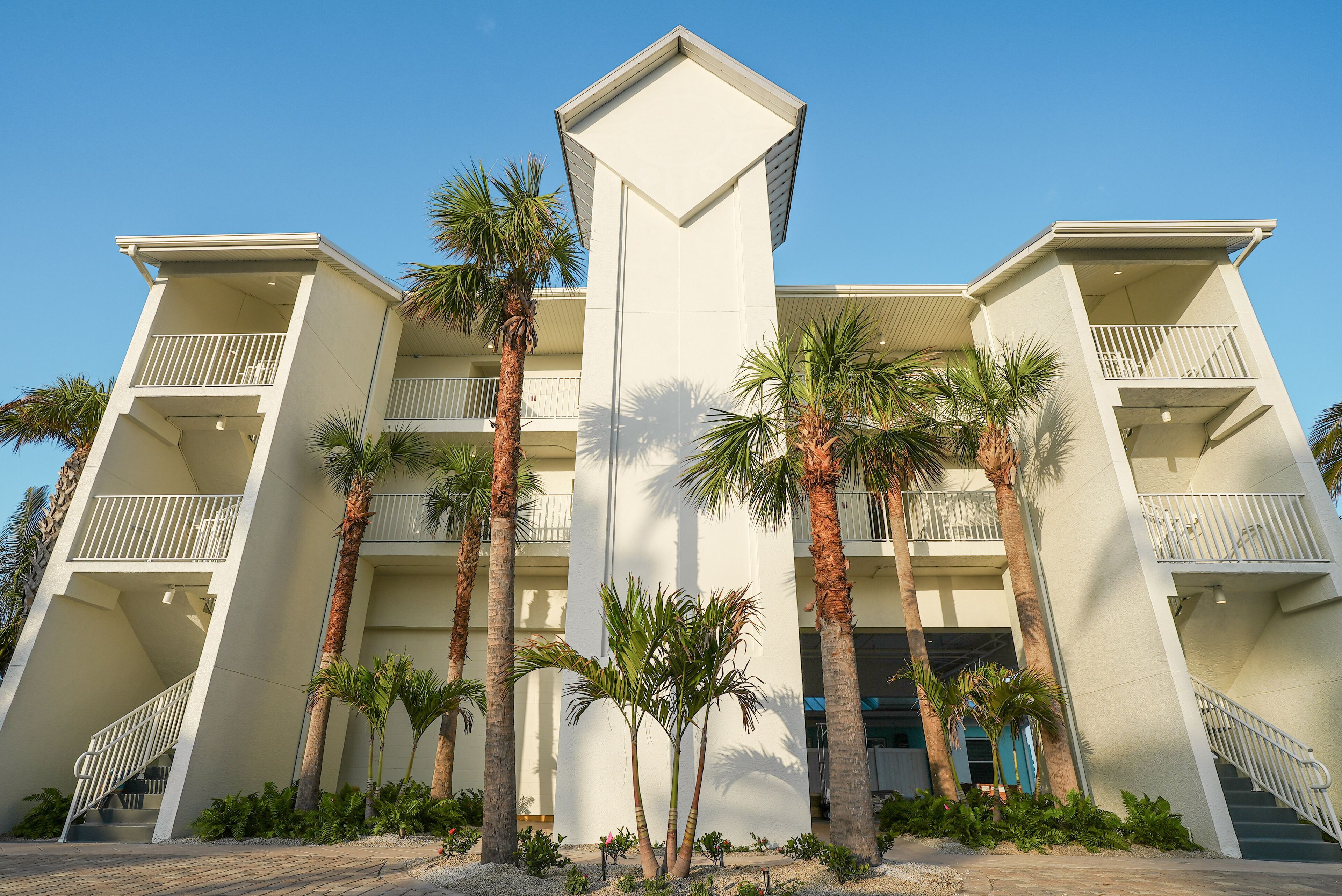 A multi-story hotel with balconies, palm trees, and a clear blue sky.