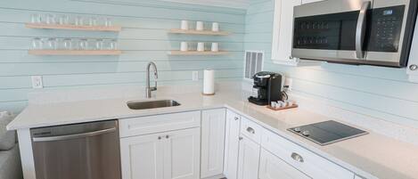A modern kitchen with white cabinetry, a stainless steel dishwasher, a built-in microwave, and a coffee maker.