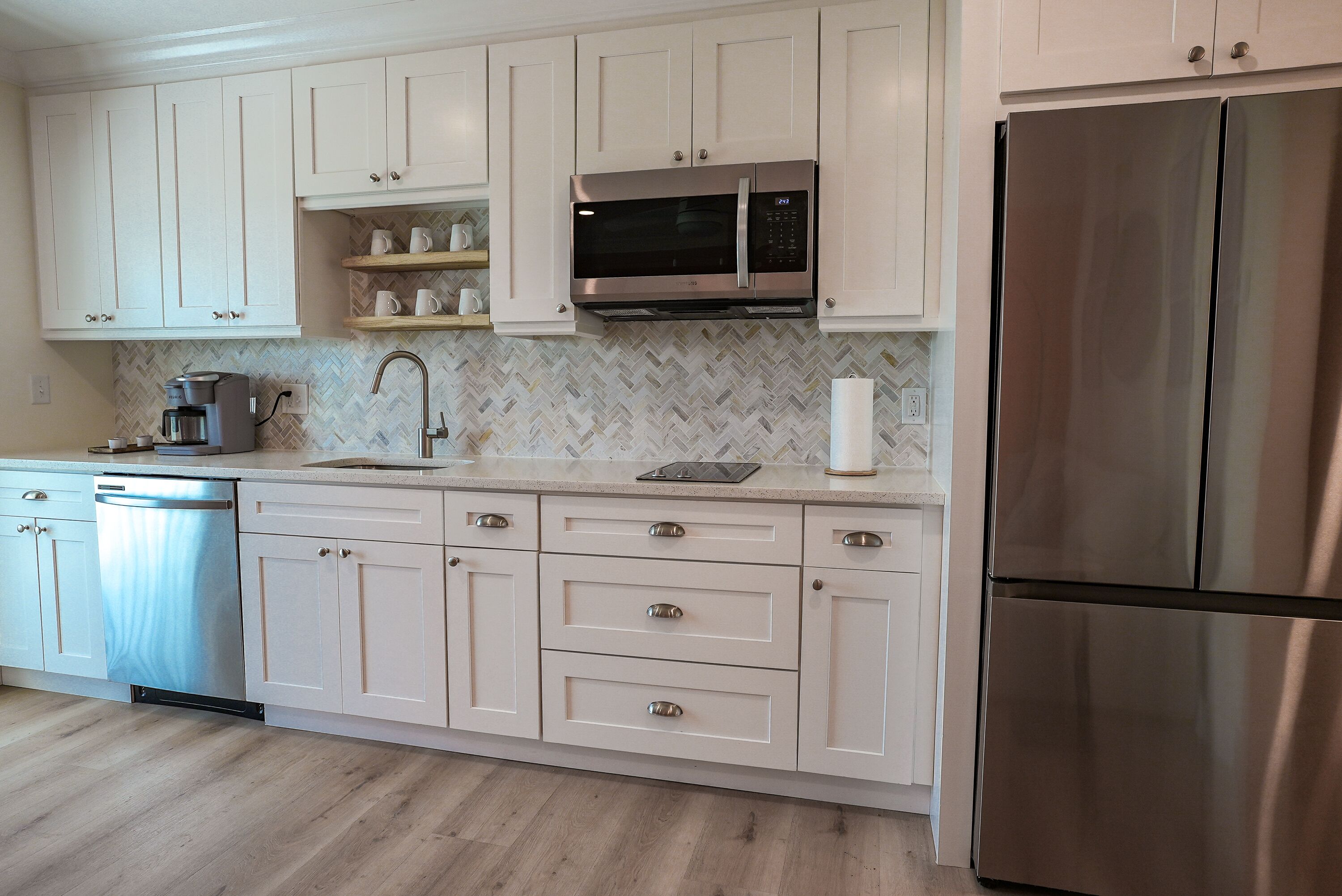 A kitchen with white cabinets, a stainless steel refrigerator, and a microwave.
