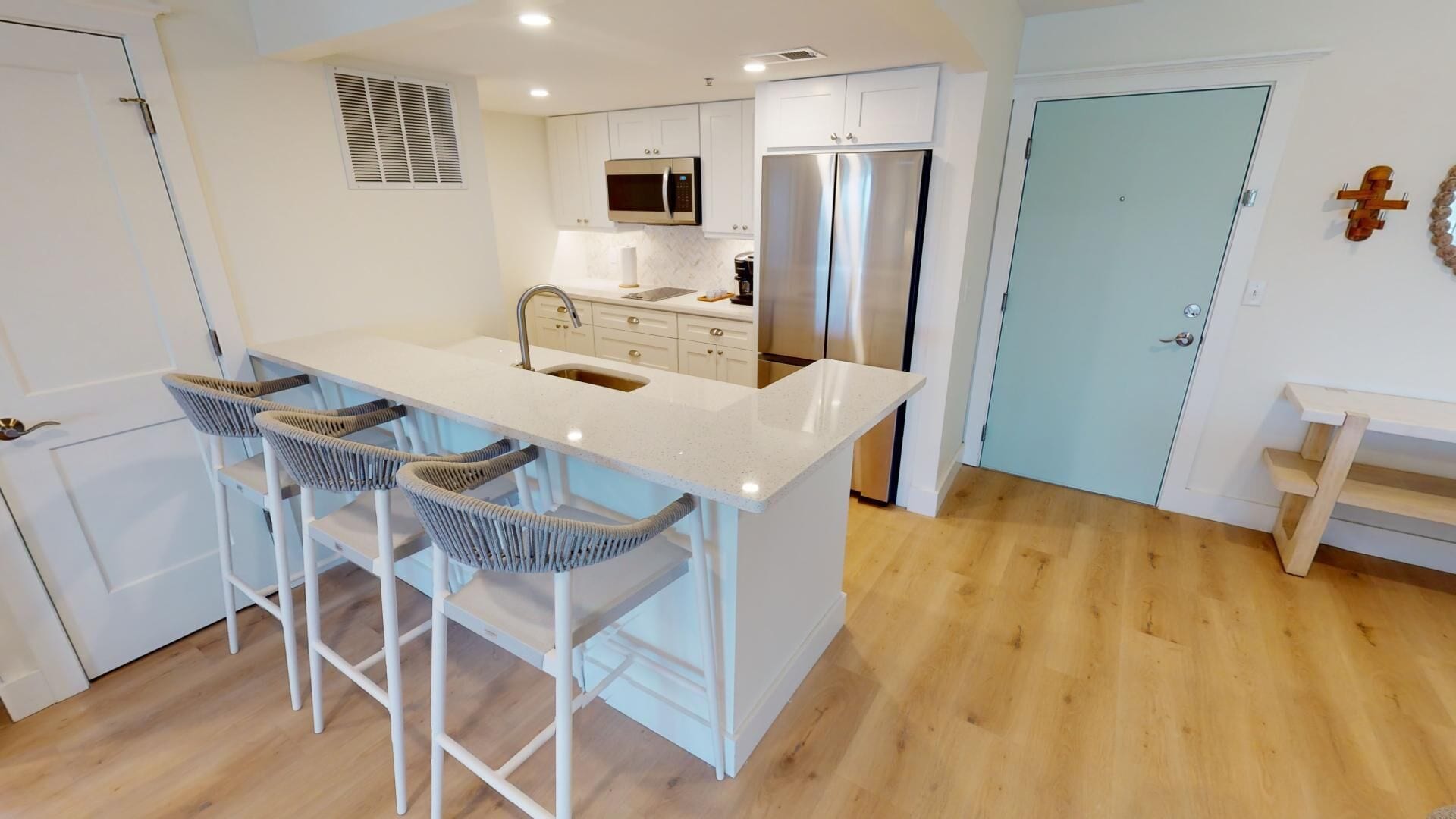 A modern kitchen with a central island, bar stools, stainless steel appliances, and light-colored cabinetry.