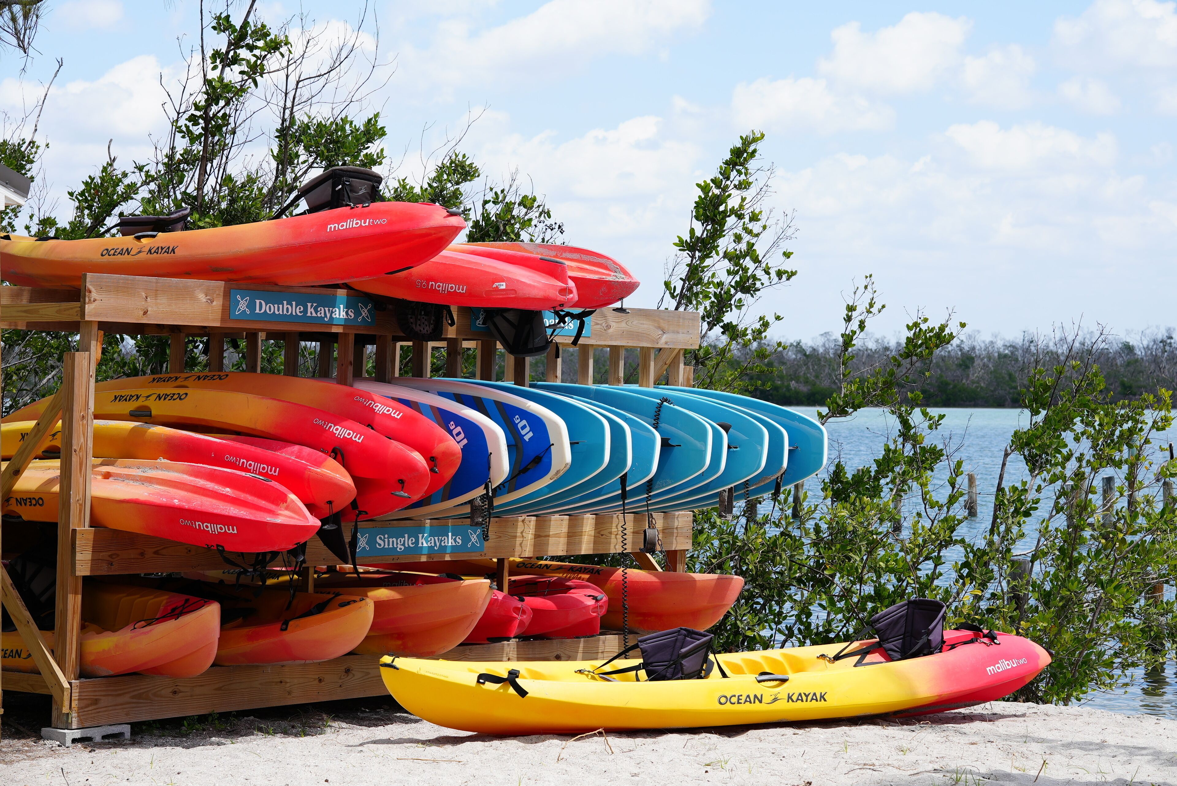 A wooden rack holding various kayaks and a single kayak on the ground.