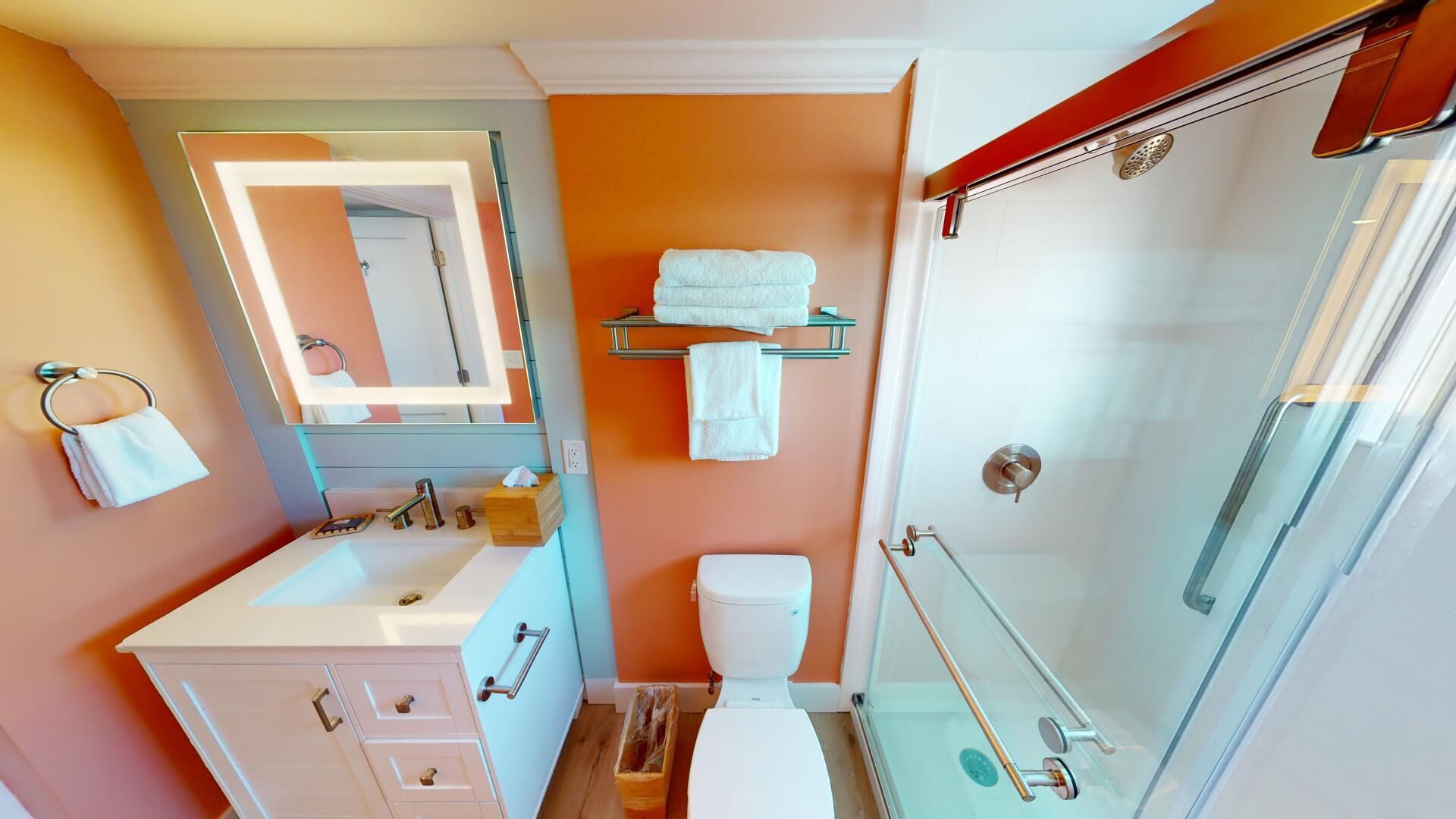 Et moderne badeværelse med en glasbrusekabine, en hvid vask og et toilet.