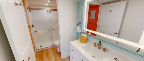 Un baño moderno con cabina de ducha de vidrio, un lavamanos blanco con detalles dorados y un espejo grande.