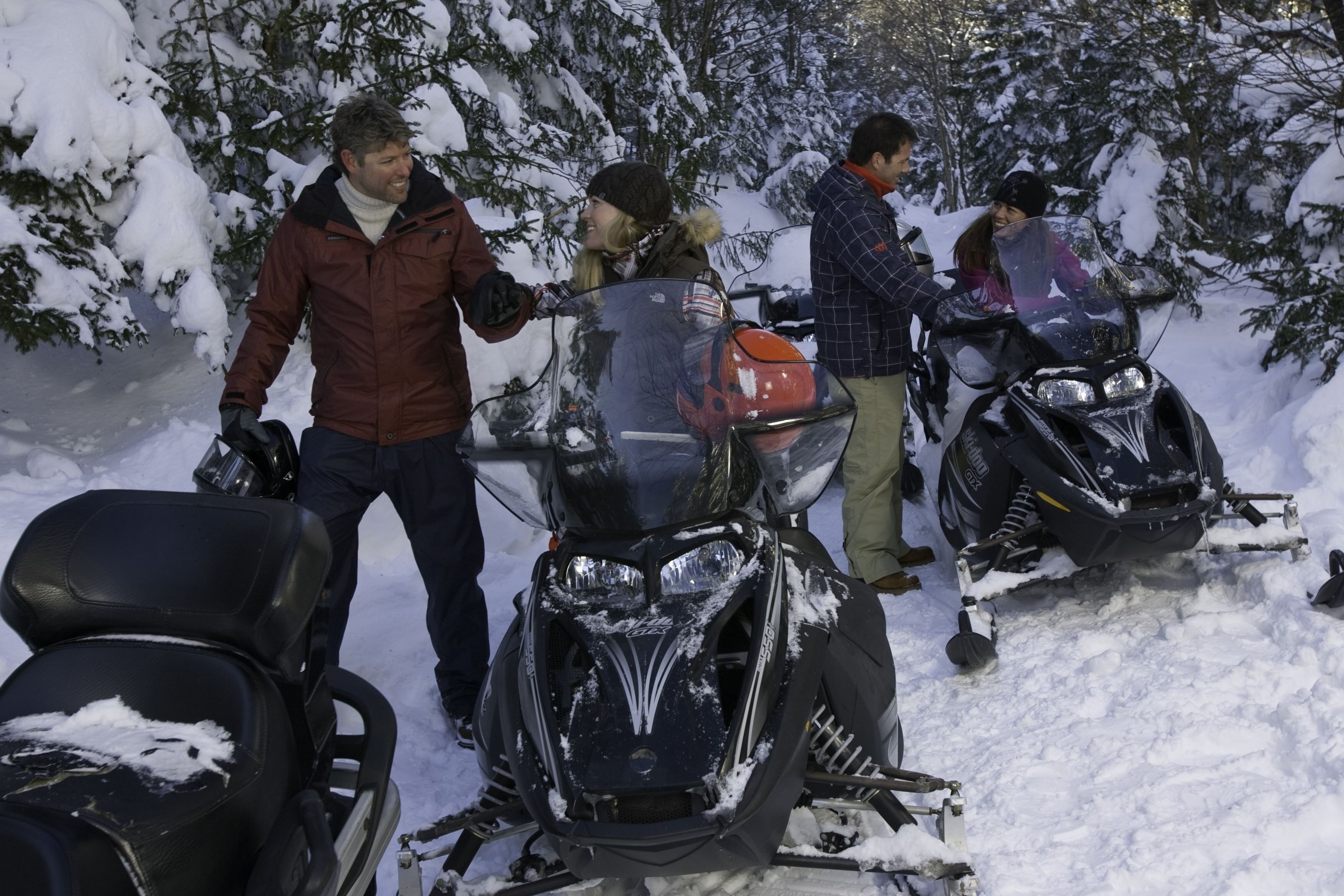 A group of people around snowmobiles in a snowy outdoor setting.