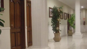 A hallway with white columns, wooden doors, and potted plants. - Scala Hotel (Lagos de Moreno)