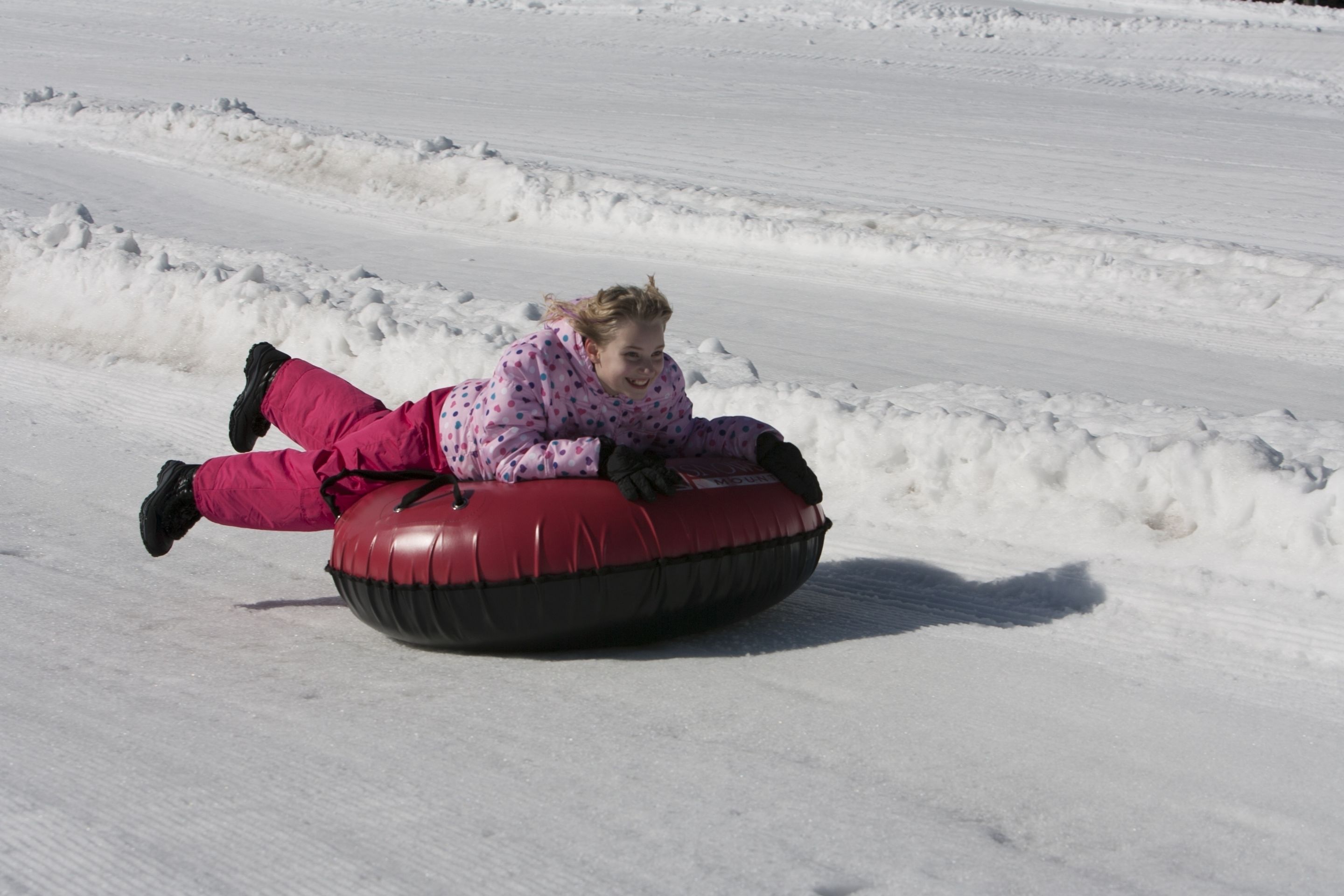 Una persona con un traje de nieve rosa con lunares surfeando un tubo de nieve rojo en una pendiente nevada.
