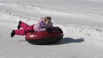 Una persona con un traje de nieve rosa con lunares surfeando un tubo de nieve rojo en una pendiente nevada.