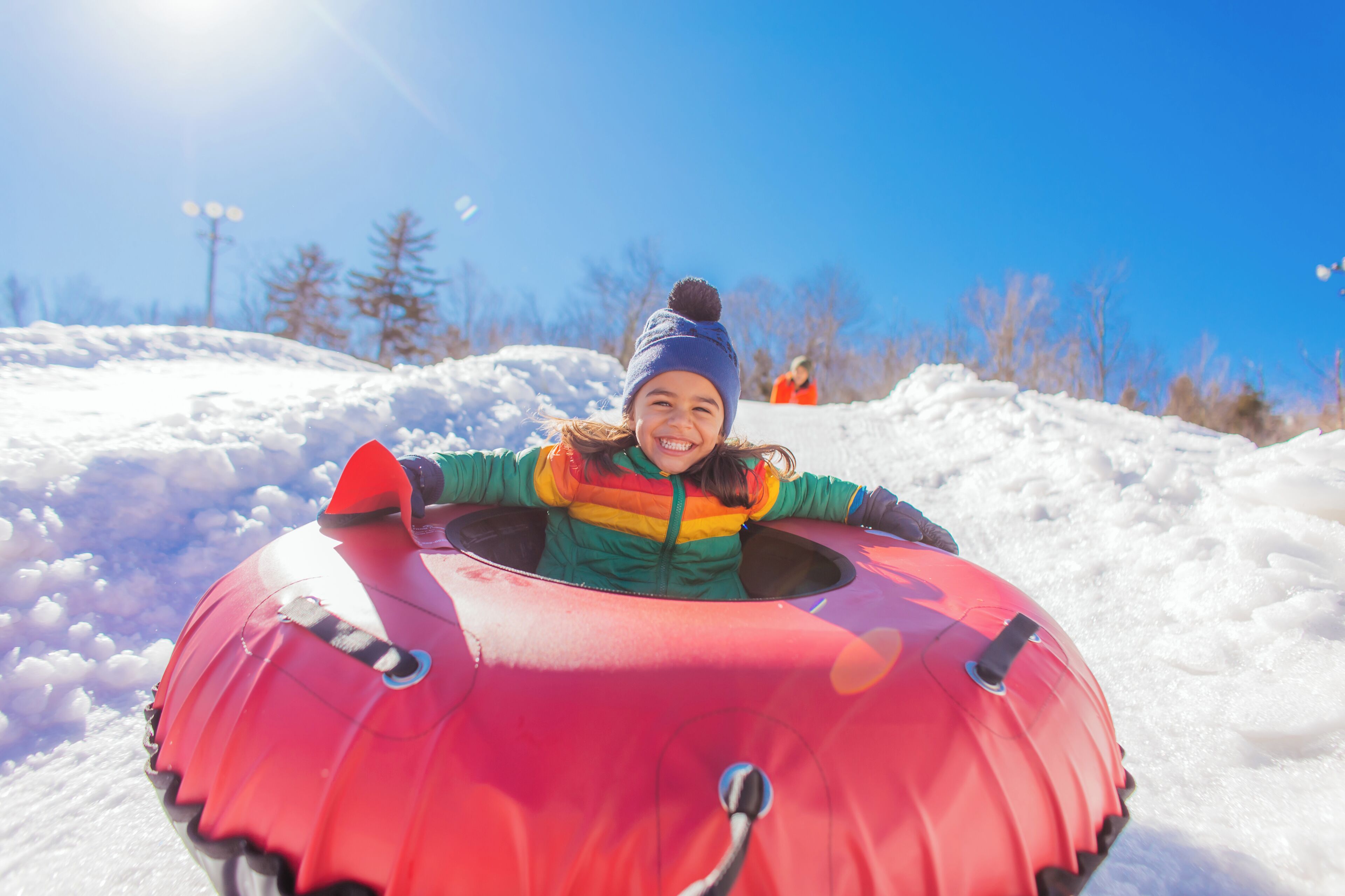 A person in a colorful jacket and hat sitting in a red sled on a snowy slope.