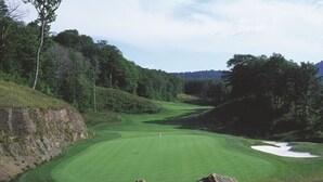 Un parcours de golf avec un gazon bien entretenu, des bunkers de sable et un mât de drapeau.